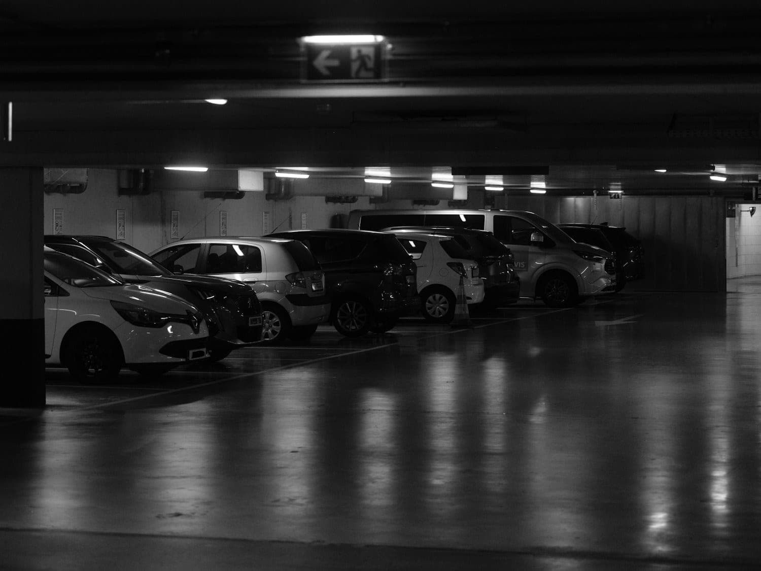 Row of cars parked in a dimly lit underground garage with a wet, reflective floor