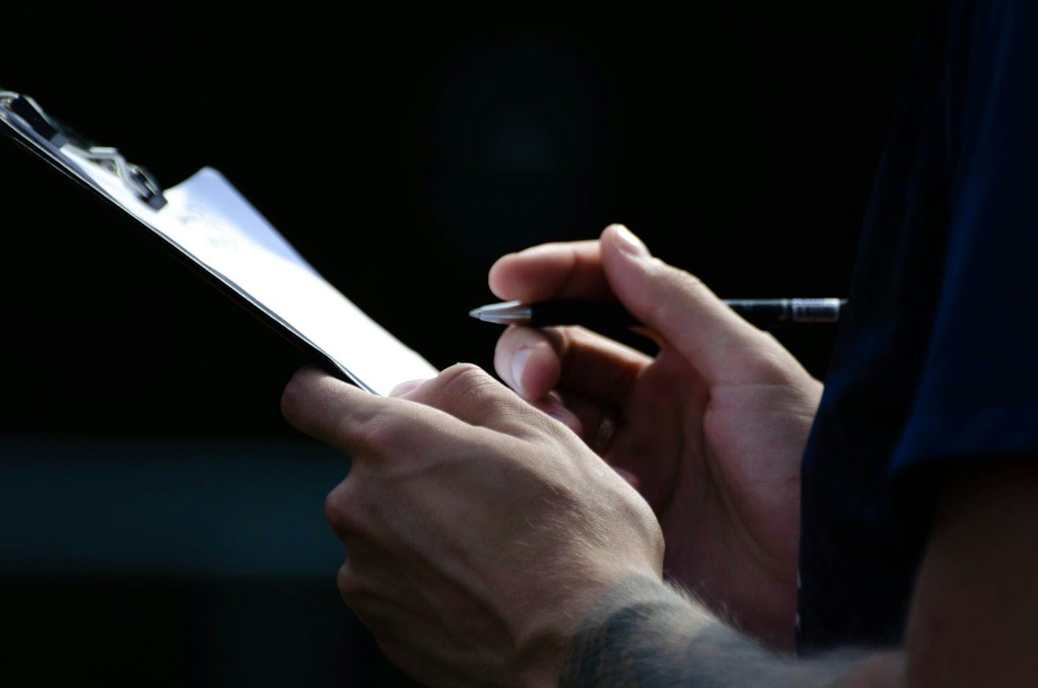 Hands writing notes on a clipboard against a dark background