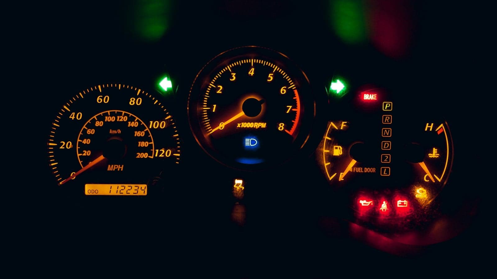 Car instrument cluster glowing orange at night with several dashboard warning lights lit