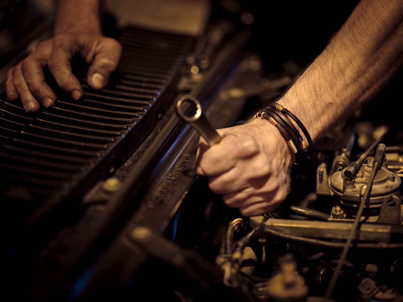 Mechanic's grease-marked hands working inside an engine bay with a wrench