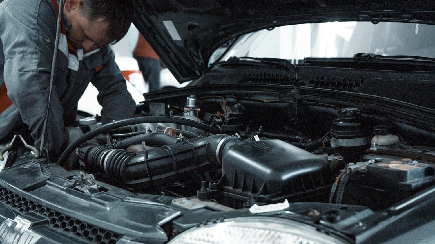 Mechanic leaning over an open hood to inspect the engine