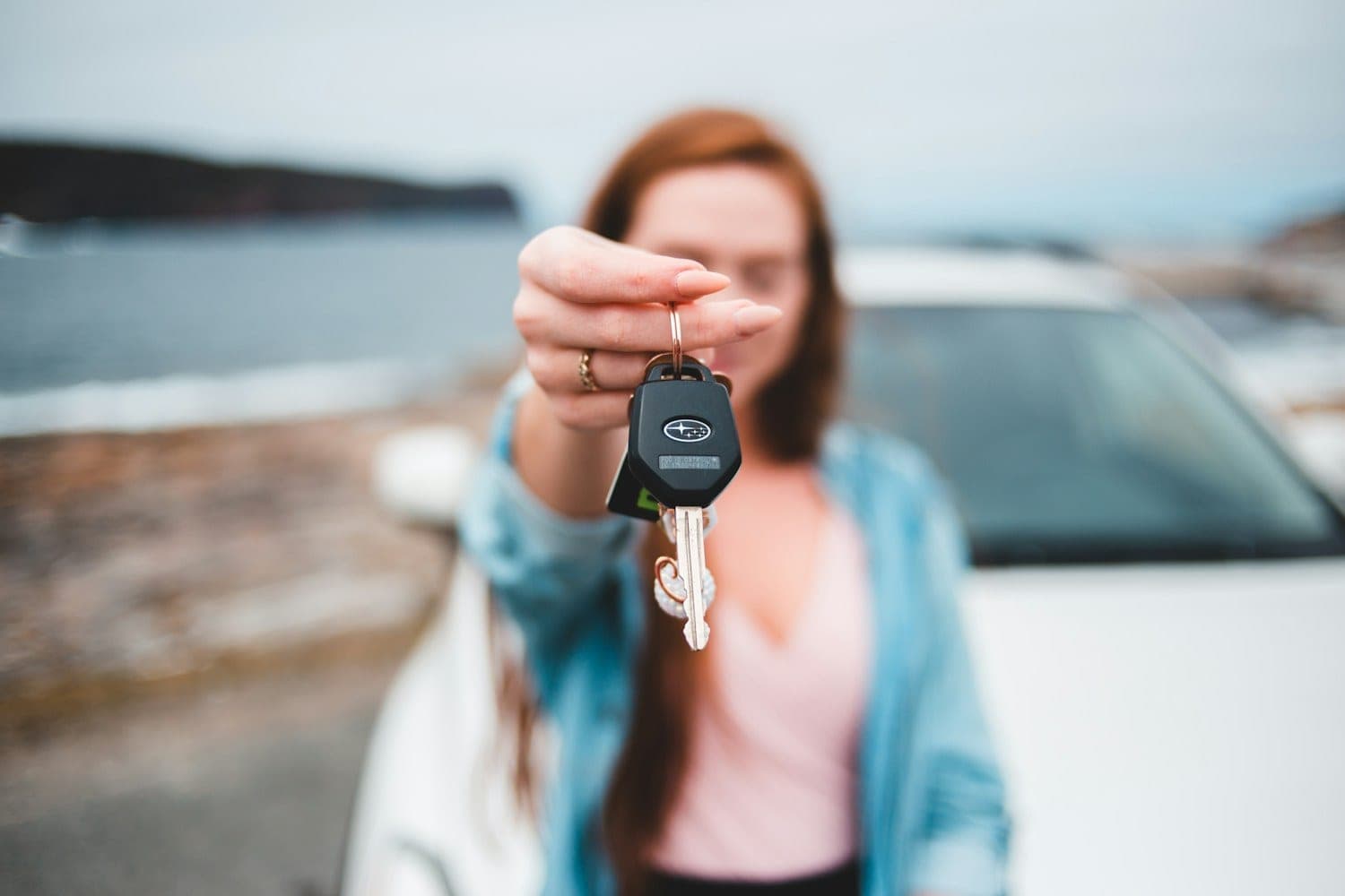 Woman holding up a car key in front of a white car