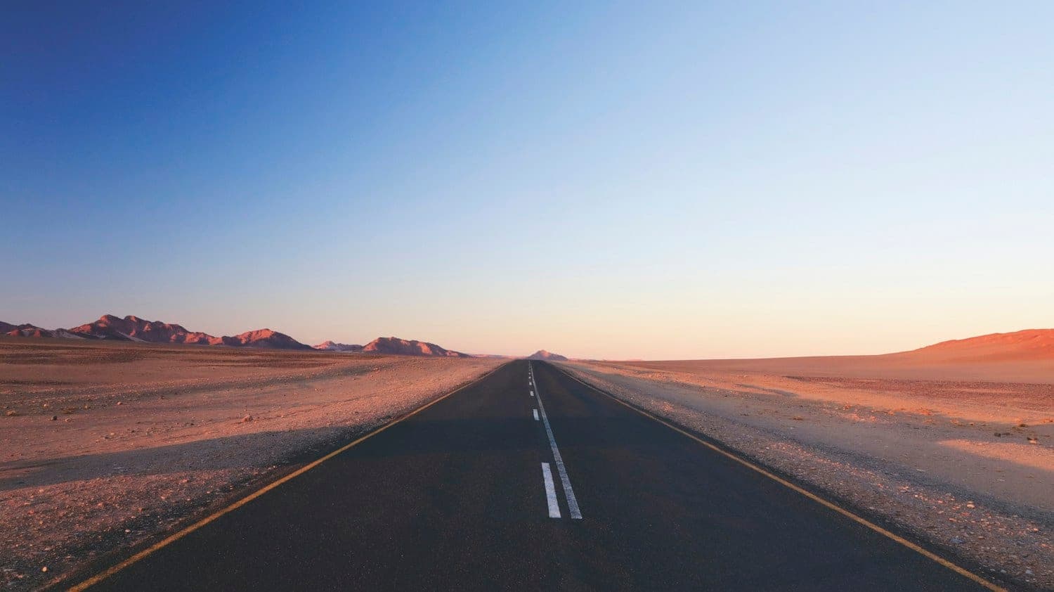 Empty two-lane road running straight through open desert at dusk