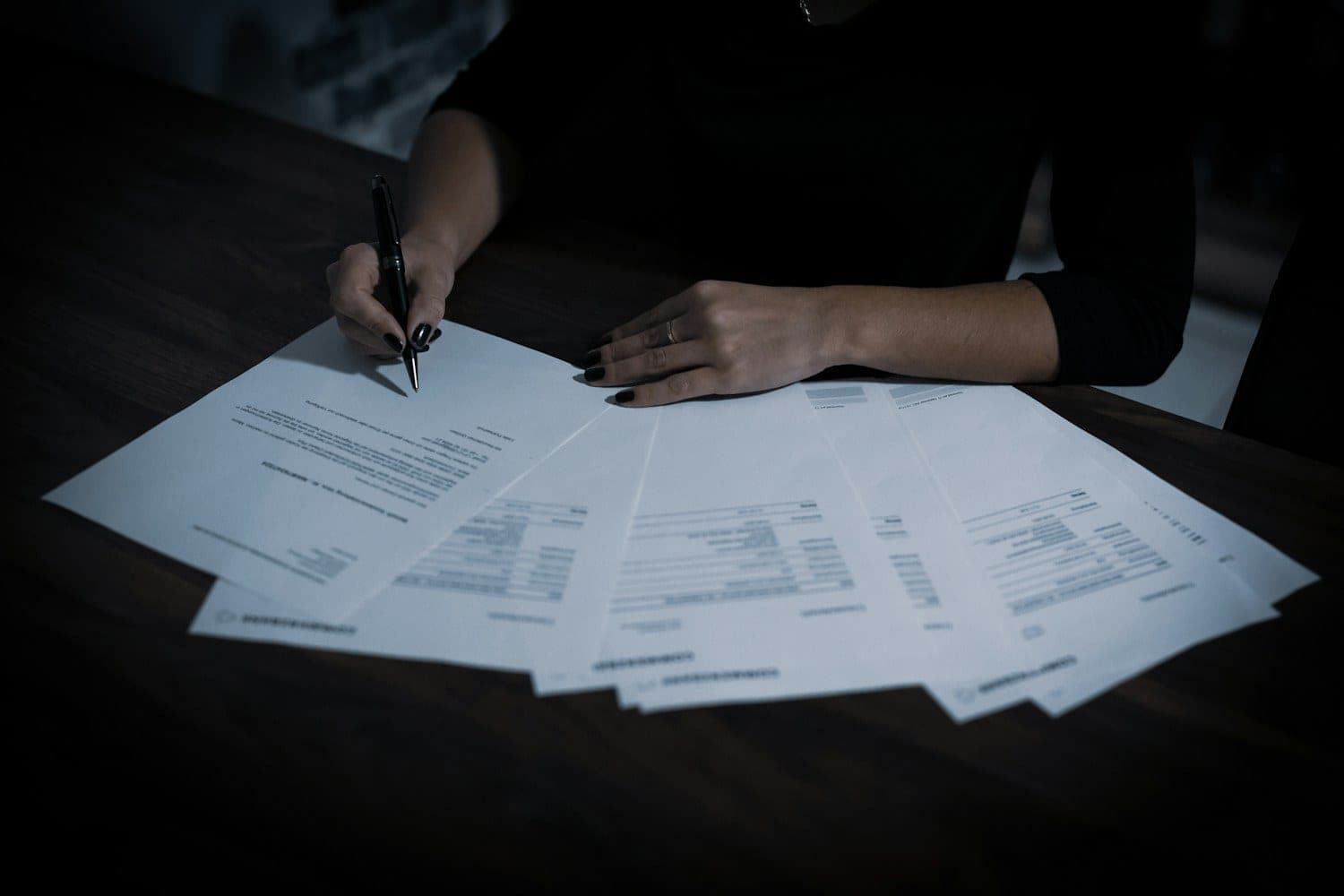 Person reviewing printed documents with a pen at a dark desk
