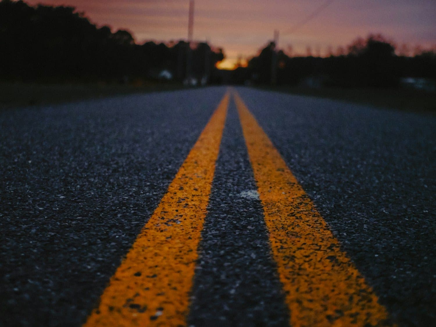 Low view along the double yellow center line of a road at dusk