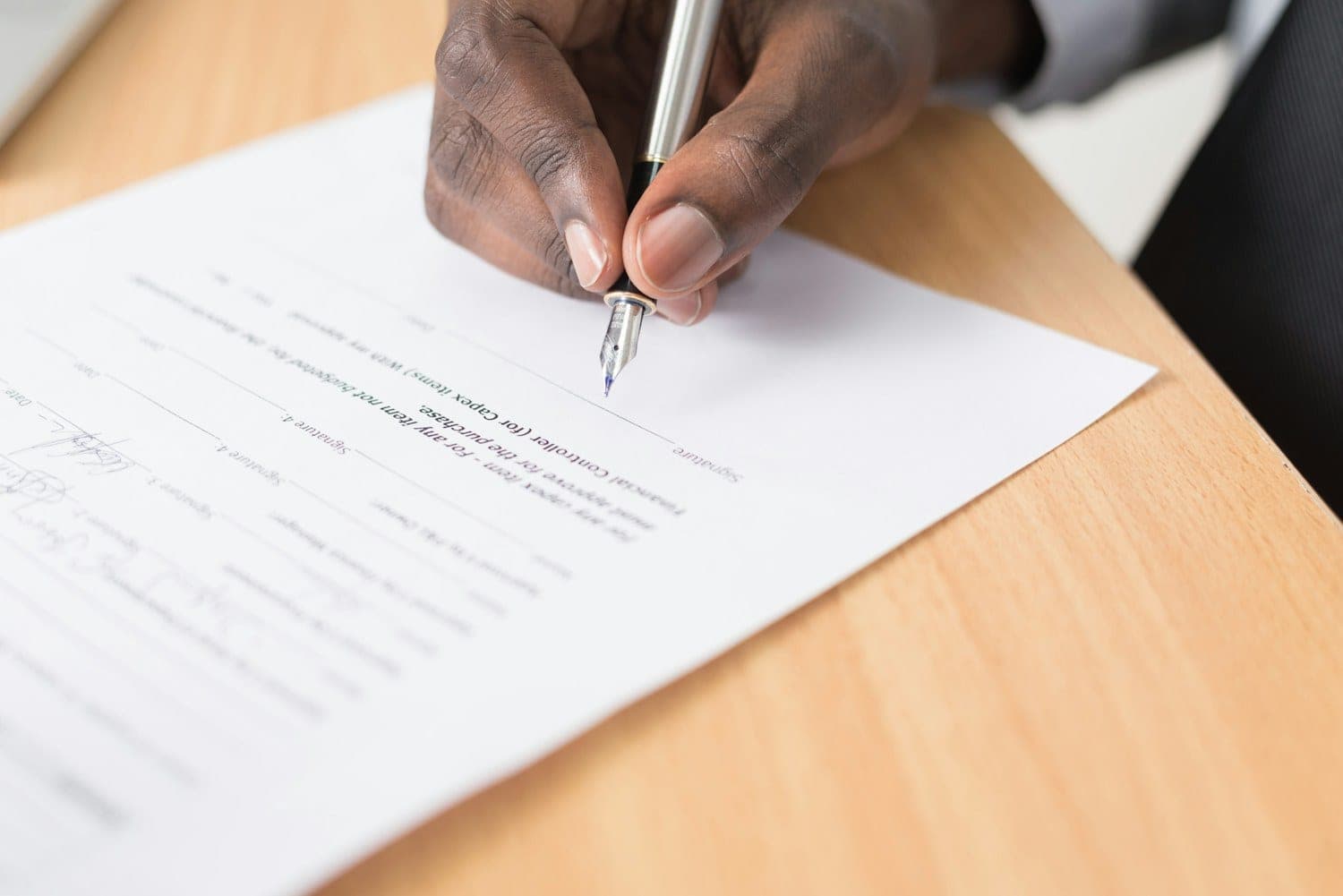 Person signing a document with a pen at a wooden desk
