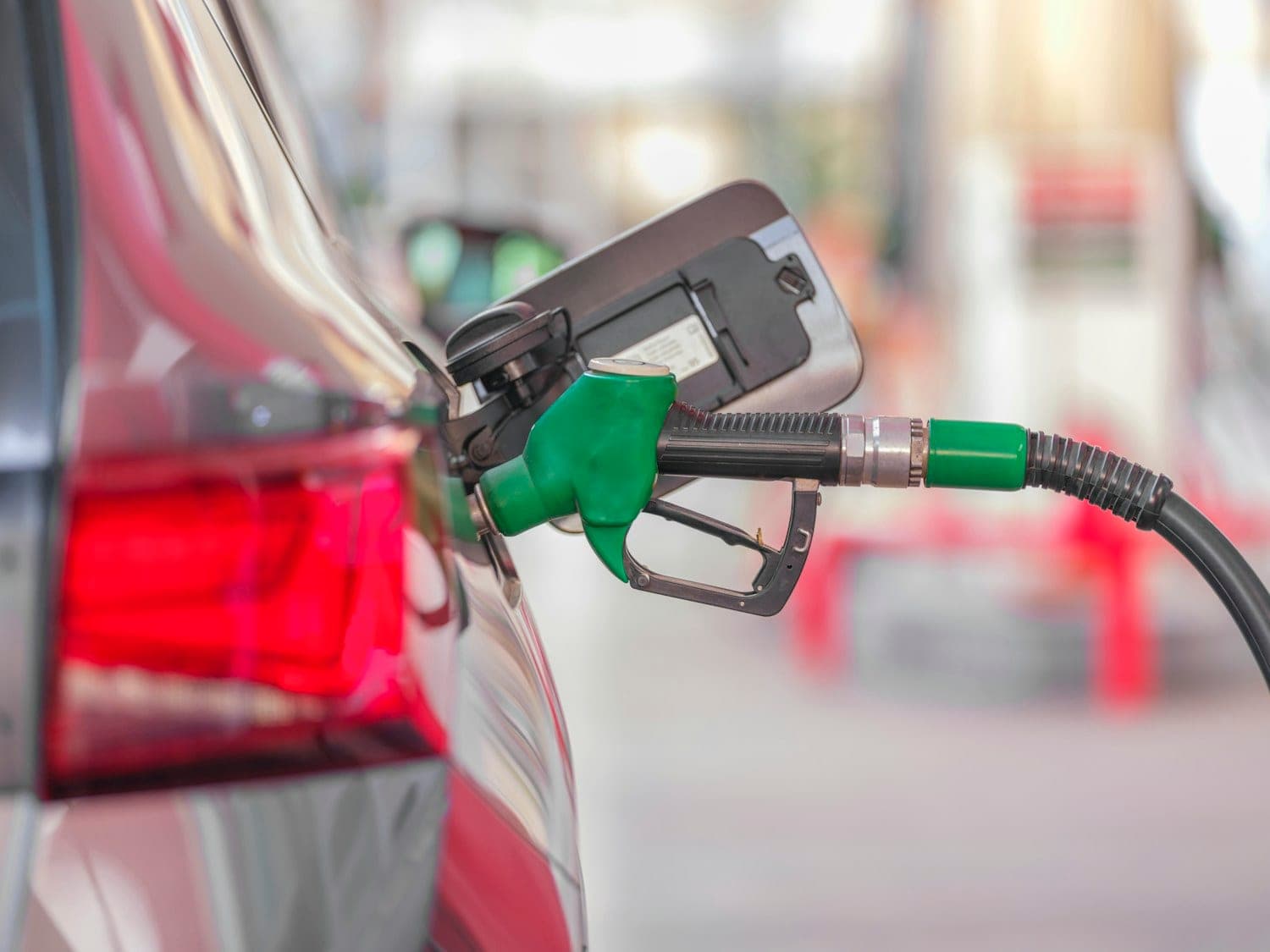 Refueling at the pump Green fuel nozzle refueling a red car at a gas station