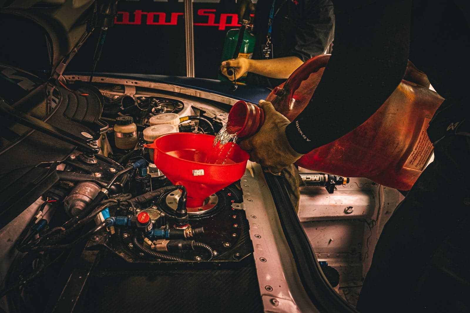 Topping up engine fluid through a funnel Fluid being poured through a red funnel into a car engine during routine maintenance